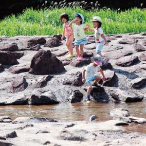 川のそばにある岩場で遊んでいる子どもたちの写真