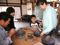 ろくろを使って陶芸体験を行っている家族の写真