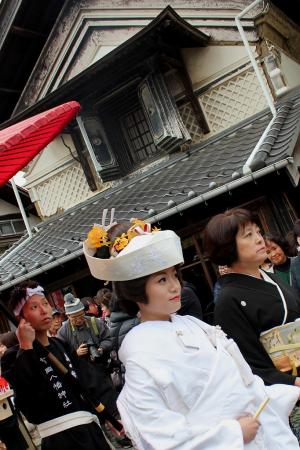 和屋敷を背景に白無垢姿の女性が花嫁道中をしているのを斜めに写した写真