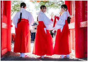 吉岡八幡神社の門で、花嫁道仲に参列する三人の巫女が後ろを振り返って笑顔で写っている写真