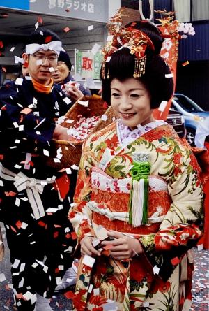 日本髪で華やかな着物を着た女性が紙吹雪の中で笑顔を浮かべている写真