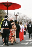 巫女や袴を履いた人の後ろで男性の差した赤い傘の下で歩いている着物の女性の写真