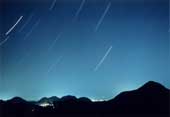 連なる山々の上の青い夜空に流れ星がたくさん降っている写真