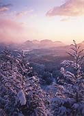 オレンジ色の空と、太陽に照らされる雪の積もった山や木々を写した写真