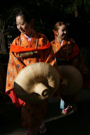 オレンジ色の着物を着て藁でできた帽子を持って歩いている二人の女性の写真