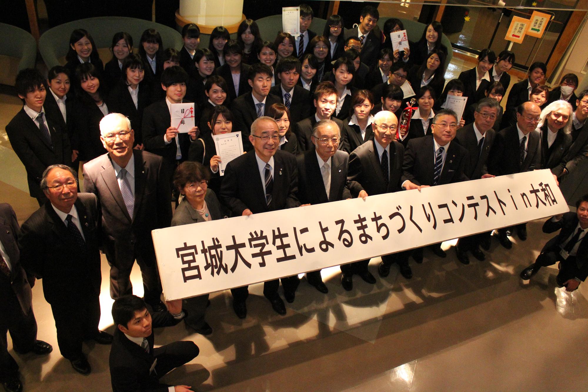 「宮城大学生によるまちづくりコンテストin大和」と書かれた横断幕を手に持った参加者たちの集合写真